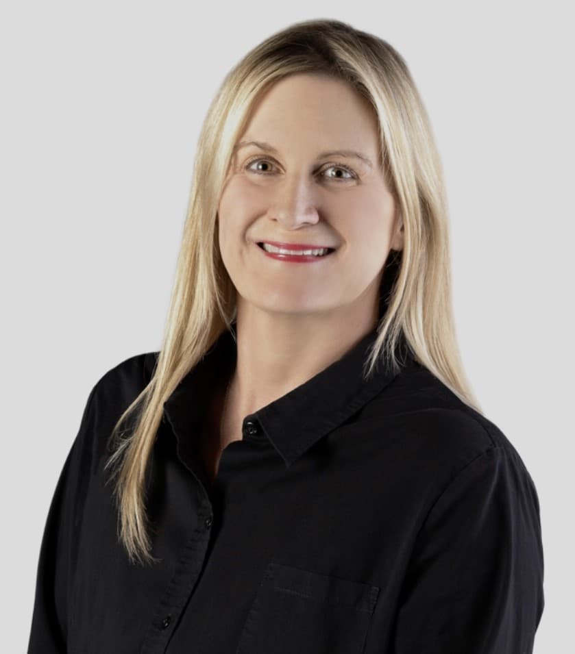 Margo Pipkorn smiling, with long blonde hair, wearing a black button-up shirt against a light grey backdrop