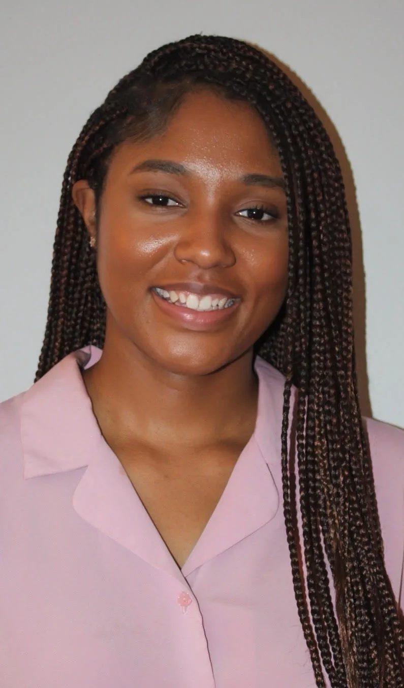 Vanessa Mallory smiling, with long dark box braids, wearing a pale pink collared blouse against a light grey wall