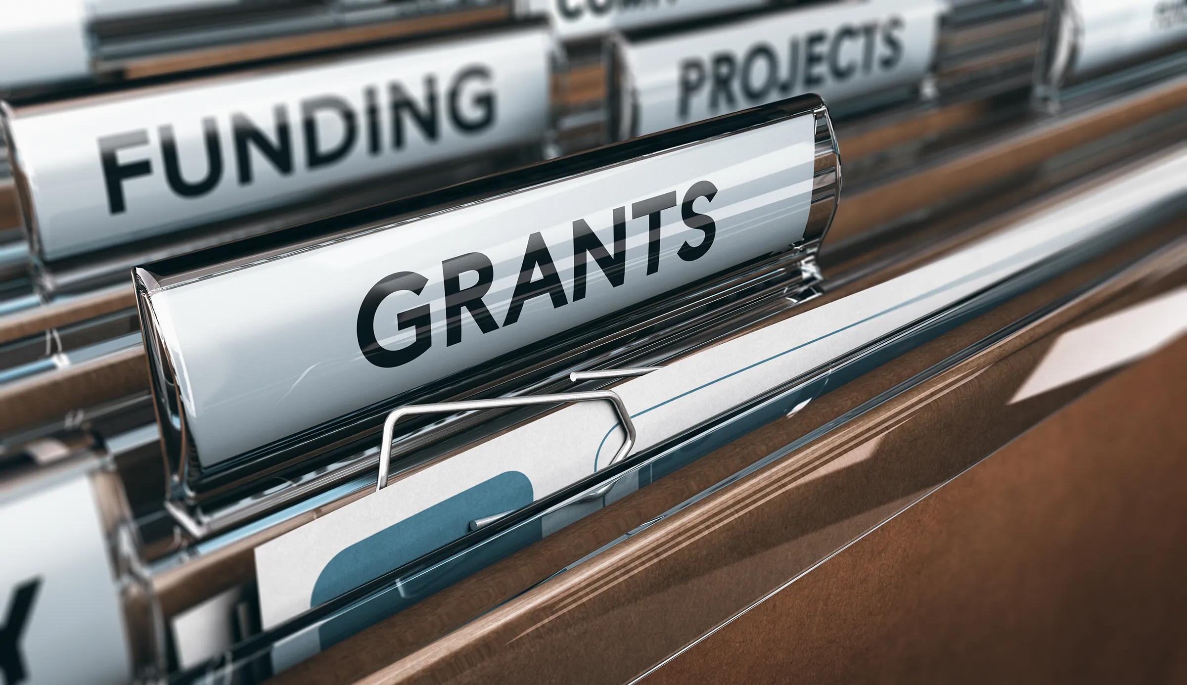 Close-up of a hanging file folder tab labelled GRANTS in sharp focus, with tabs labelled FUNDING and PROJECTS blurred behind it