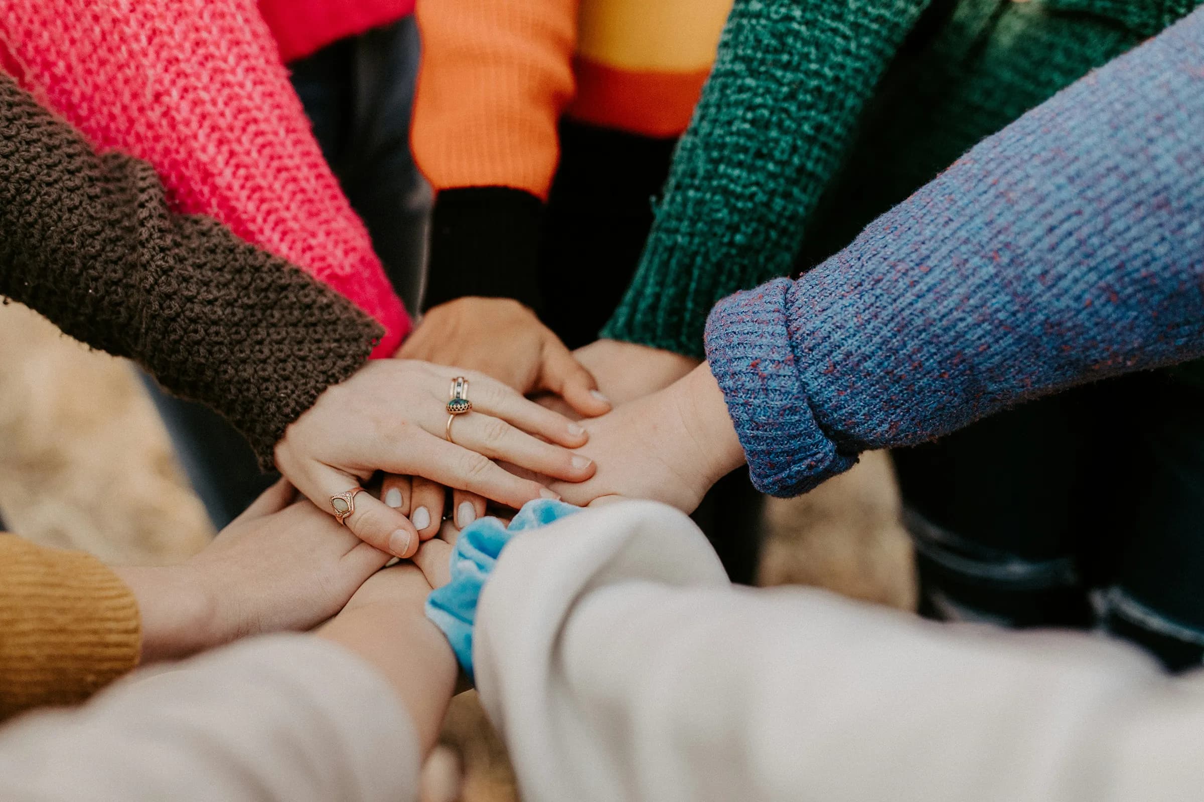 Close-up of a circle of people in colorful knit sweaters stacking their hands together in the middle