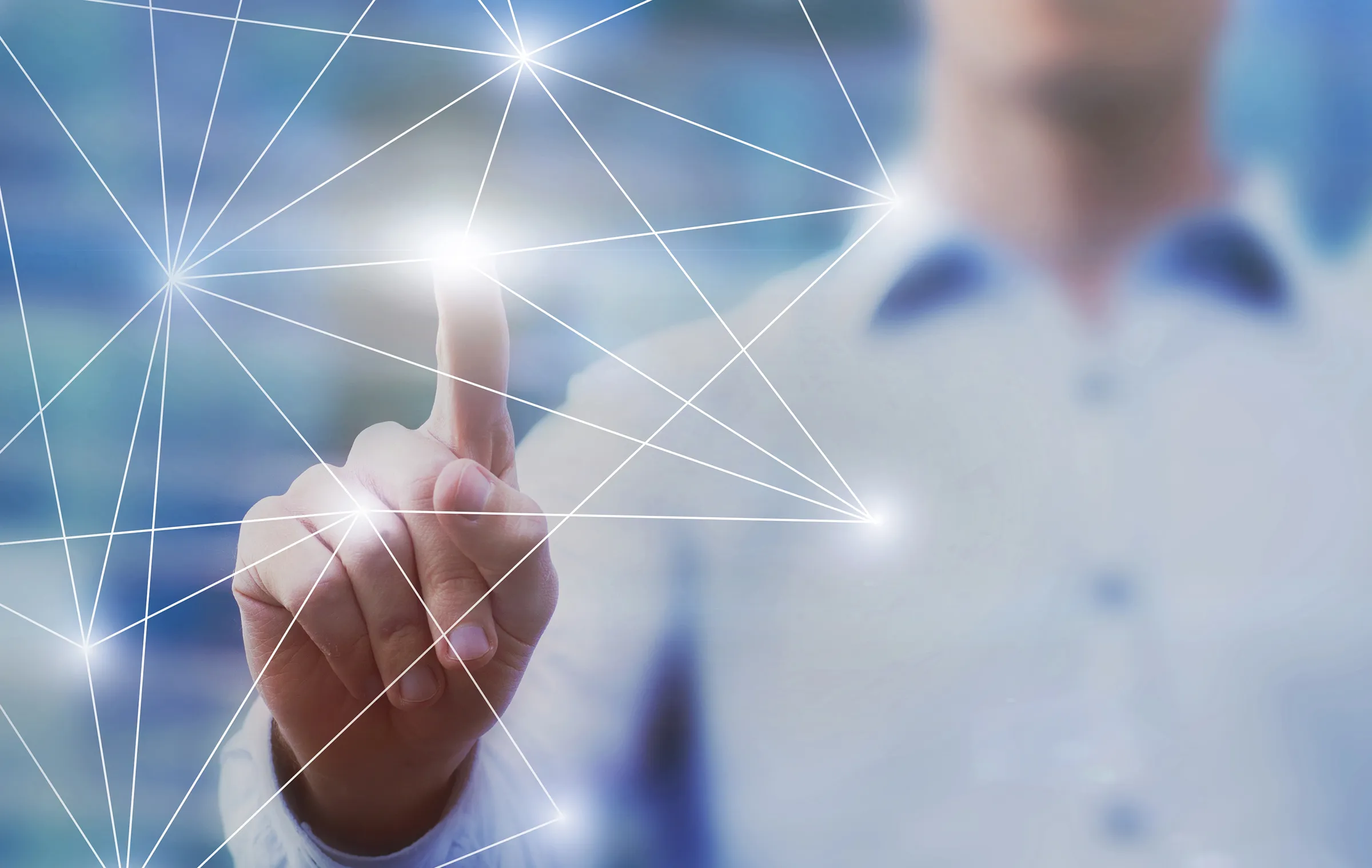 A person in a light button-down shirt, blurred in the background, touches one glowing node of a white network of connected lines with an index finger against a soft blue backdrop