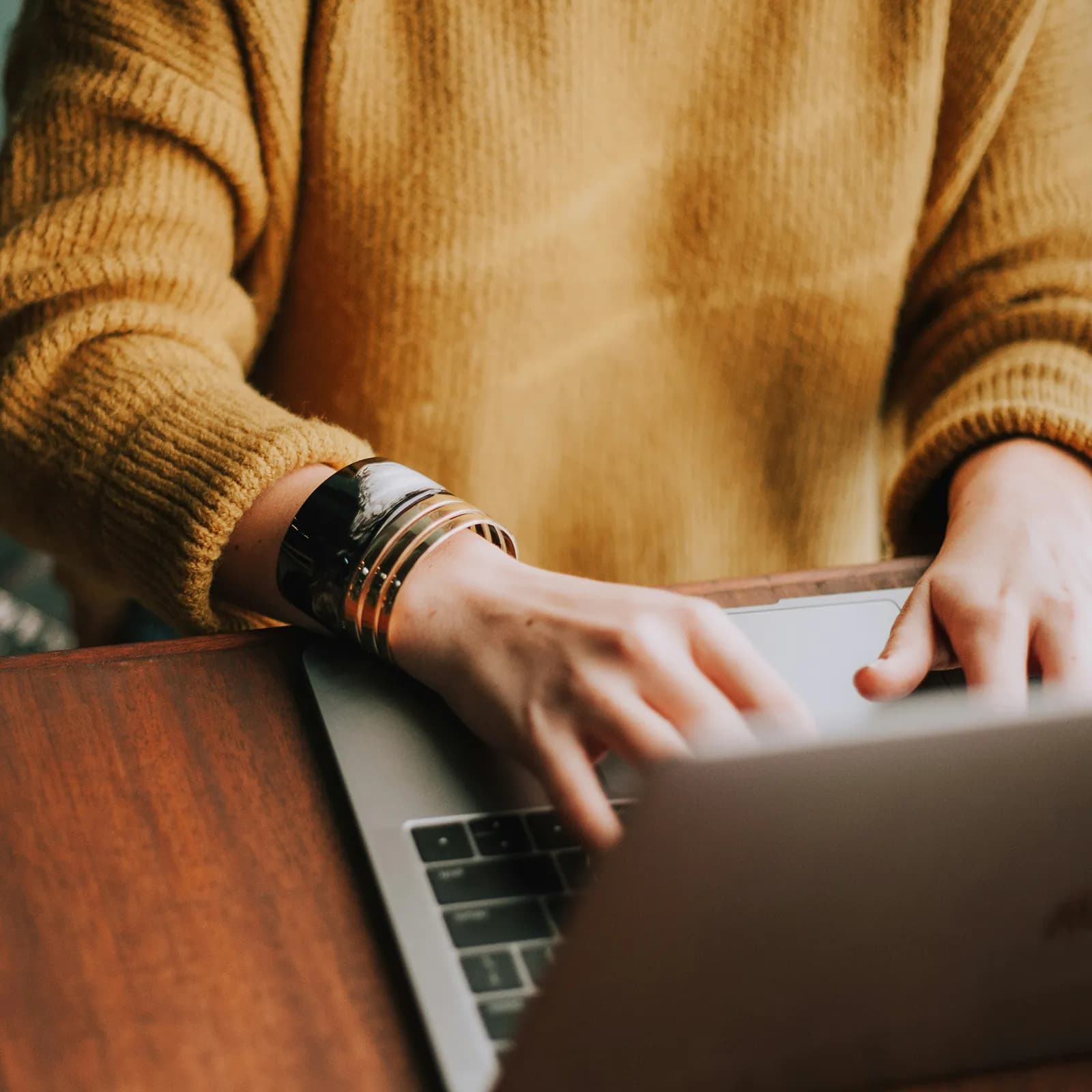 Close-up of a person in a mustard sweater and stacked bangles typing on a laptop