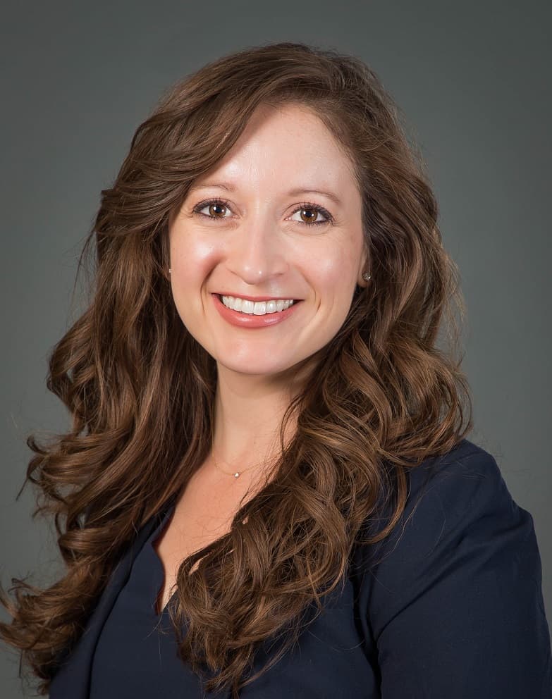 Stephanie Halvorson smiling, with long wavy brown hair, wearing a navy top against a grey backdrop