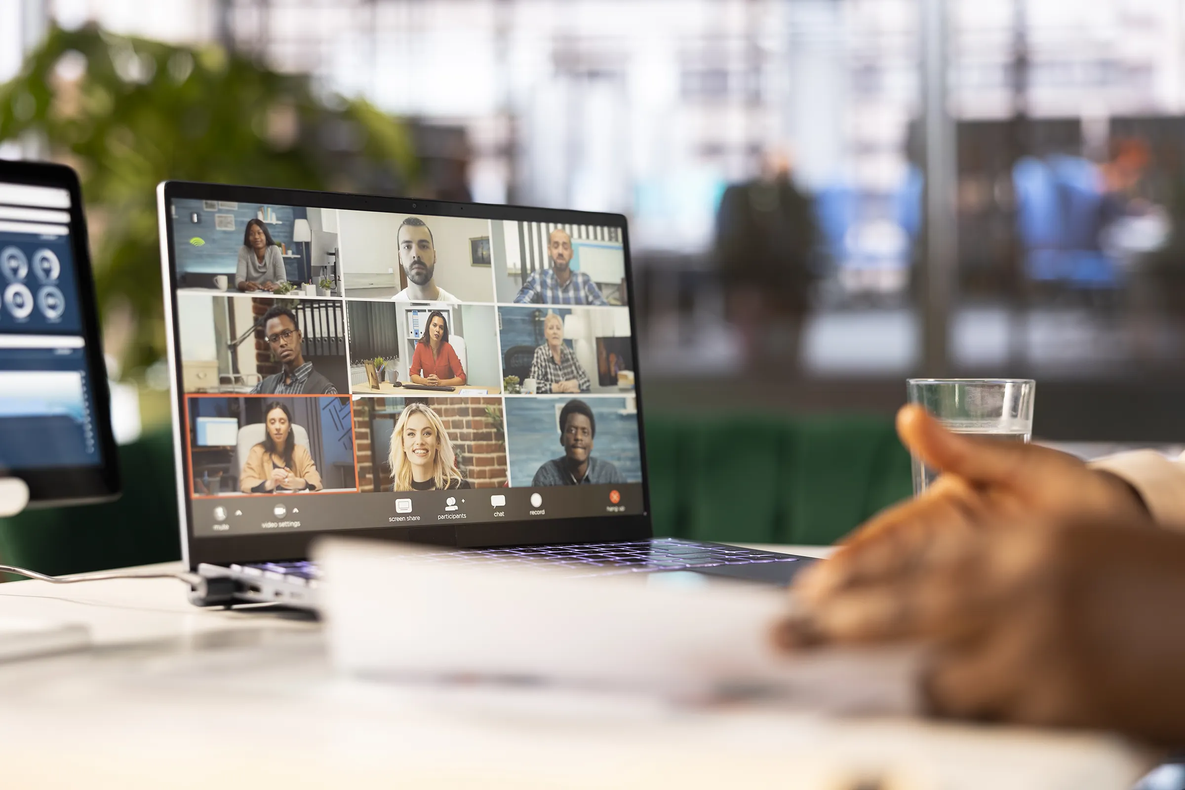 A laptop on a desk showing a video call with a grid of nine participants